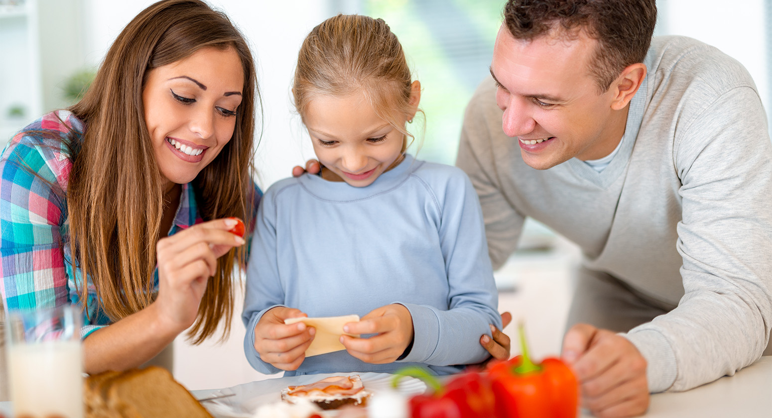 Its Cool - A importância do estímulo a educação alimentar na infância. Casal com sua filha, sorrindo enquanto estão mexendo com alimentos na mesa