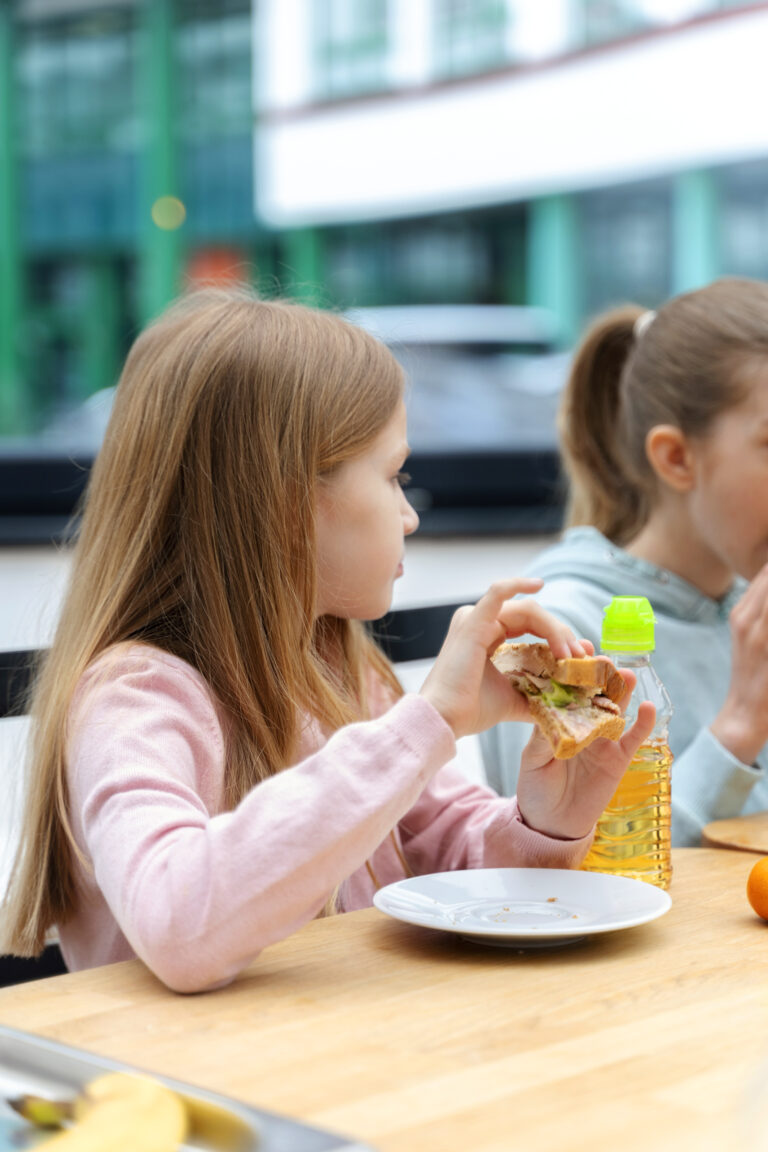 criança de perfil sentada à mesa com um sanduíche na mão