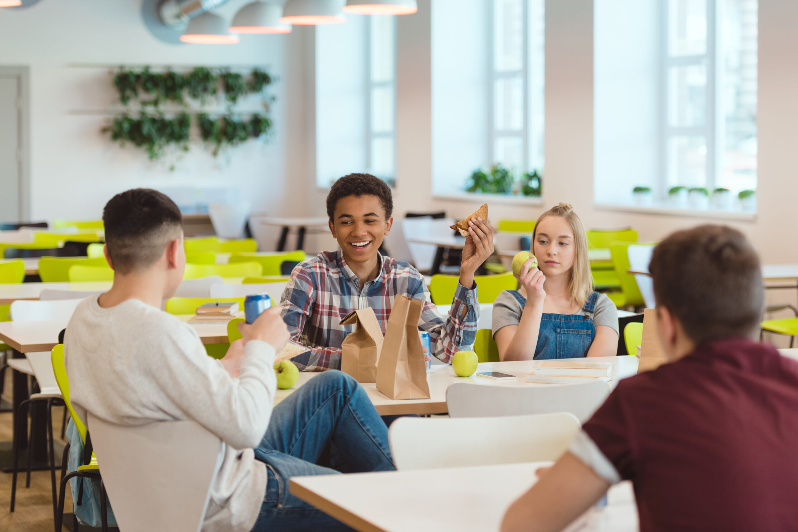 Imagem com adolescentes sentados em um refeitório conversando e comendo..