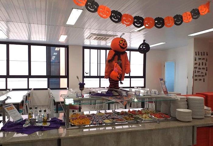 Restaurante escolar It’s Cool com decoração de Halloween e buffet com lanches saudáveis e coloridos.